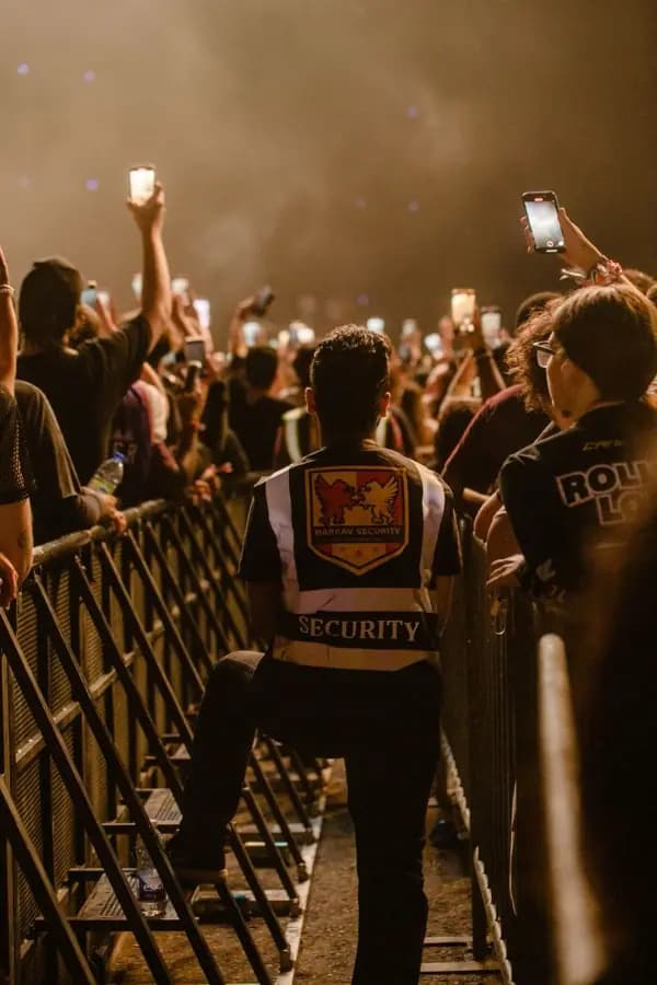 A steward in a marked Security jacket at a crowd barrier during a night event