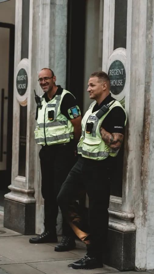 Two security officers in high-visibility vests on the door of an office building in London