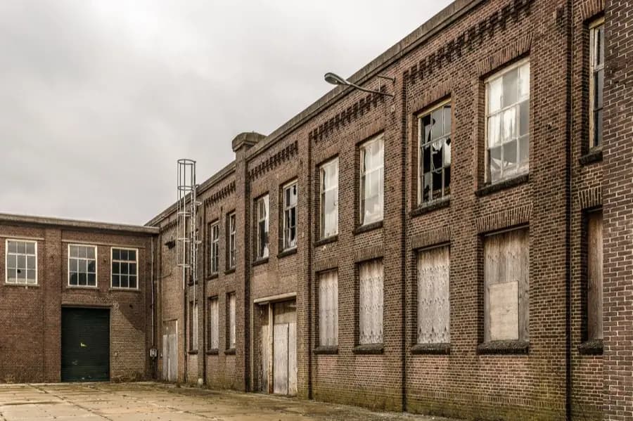 A derelict brick industrial building with boarded and broken windows